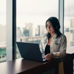 Woman wearing headphones working on a laptop by window